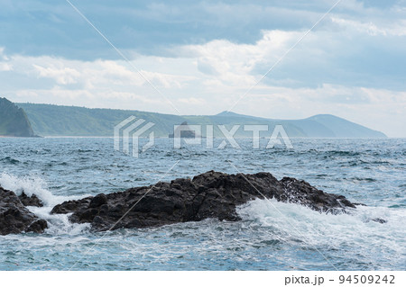 seascape with distant wooded shore on a background and rocks in the surf on a foreground, Kunashir island landscape 94509242