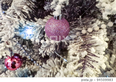 Purple shiny balls on the Christmas tree. White pearl beads on spruce branches. The branches are covered with frost. Christmas or New Year background 94509983