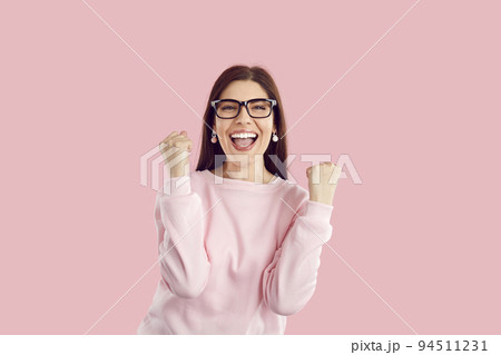 Happy excited woman rejoices success, clenched fists and triumphantly exclaims on pink background. 94511231