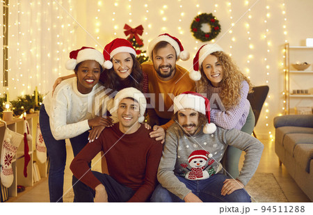 Portrait of cheerful young friends in Santa hats posing in cozy living room with Christmas decor. 94511288
