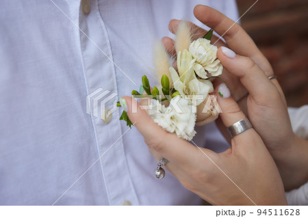 The hands of the newlyweds with gold rings close-up against the background of a plaid jacket with a boutonniere. 94511628