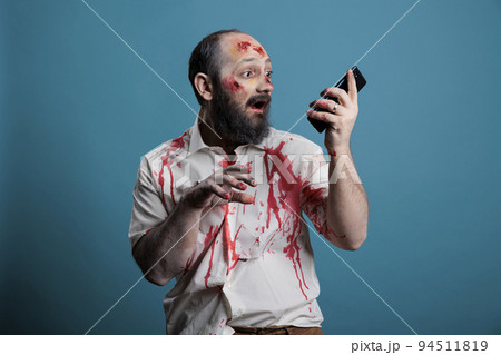 Spooky halloween monster holding smartphone in studio, using mobile phone app while being aggressive and scary. Frightening undead zombie with bloody wounds, cruel corpse with telephone. Spooky halloween monster holding smartphone in studio, using mobile phone app while being aggressive and scary. Frightening undead zombie with bloody wounds, cruel corpse with telephone. 94511819