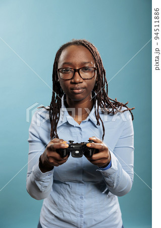 Smiling fun woman playing online videogames on gaming console with controller on blue background. Young adult person enjoying leisure time by playing games with gaming gamepad 94511886