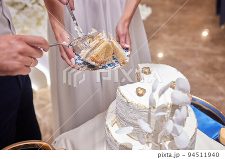 The bride and groom at the banquet together cut the wedding cake, holding on to one knife. Wedding details close-up. The bride and groom at the banquet together cut the wedding cake, holding on to one knife. Wedding details close-up. 94511940