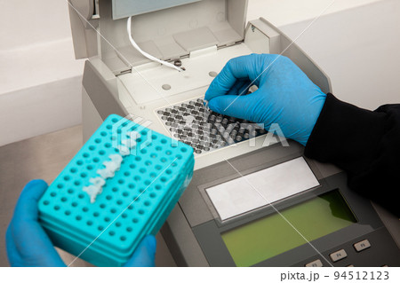 Closeup of a scientist hand while working at the laboratory with a thermal cycler. Polymerase chain reaction technique. PCR technique 94512123