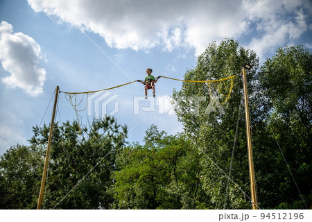 The boy is jumping on a bungee trampoline. A child with insuranc 94512196