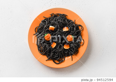 Halloween Italian black pasta decorated funny spiders in orange plate on white. 94512594