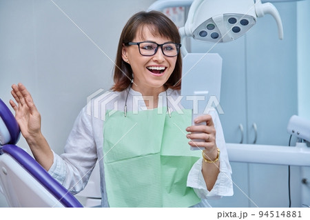 Middle-aged female in dental office looking in mirror Middle-aged female in dental office looking in mirror 94514881