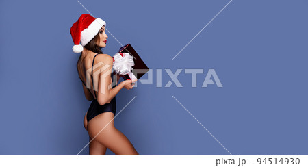 Portrait of young, sexy and beautiful woman in swimsuit and Santa hat, holding gift box. Girl in underwear lingerie. Blue background. Christmas, xmas, x-mas and winter concept 94514930