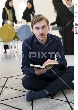 Young muslim man sitting on the floor while reading holy book Quran before iftar dinner during a ramadan feast at home 94516954