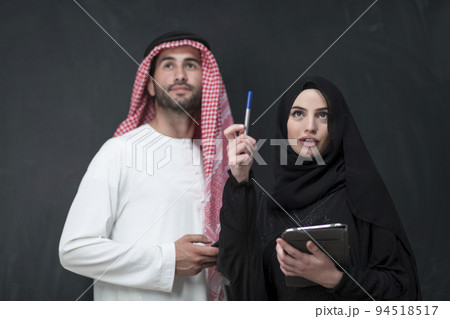 Young muslim business couple in fashionable hijab dress using smartphone and tablet in front of black background Young muslim business couple in fashionable hijab dress using smartphone and tablet in front of black background 94518517
