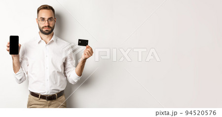 Serious business man showing mobile screen and credit card. Concept of online shopping Serious business man showing mobile screen and credit card. Concept of online shopping 94520576