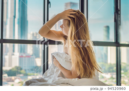 Woman wakes up in the morning in an apartment in the downtown area with a view of the skyscrapers. Life in the noise of the big city concept. Not enough sleep 94520960