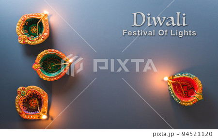Happy Diwali - Clay Diya lamps lit during Diwali, Hindu festival of lights celebration. Colorful traditional oil lamp diya on blue background 94521120