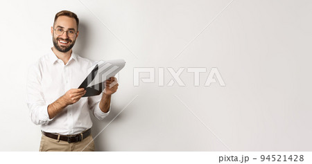 Employer looking satisfied at CV, reading document and smiling, standing over white background Employer looking satisfied at CV, reading document and smiling, standing over white background 94521428