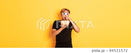 Impressed and thrilled asian guy attend cinema, watching movie or tv series in 3d glasses, eating popcorn and looking shocked, standing yellow background Impressed and thrilled asian guy attend cinema, watching movie or tv series in 3d glasses, eating popcorn and looking shocked, standing yellow background 94521572