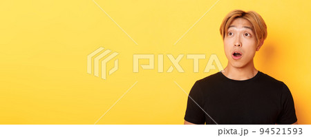 Close-up of impressed asian handsome guy, looking upper left corner with dropped jaw and amazement, standing over yellow background Close-up of impressed asian handsome guy, looking upper left corner with dropped jaw and amazement, standing over yellow background 94521593