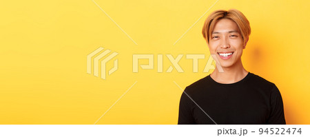 Close-up of handsome stylish asian guy with fair hair, smiling happy over yellow background 94522474