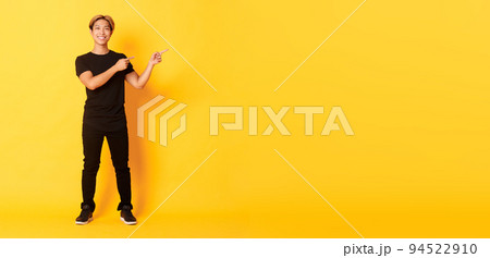 Full-length of handsome confident asian guy smiling happy, pointing fingers right, showing logo, yellow background Full-length of handsome confident asian guy smiling happy, pointing fingers right, showing logo, yellow background 94522910