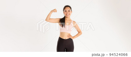 Sport, wellbeing and active lifestyle concept. Portrait of smiling slim and strong asian fitness girl, personal workout trainer showing muscles, flexing biceps and look proud, white background 94524066