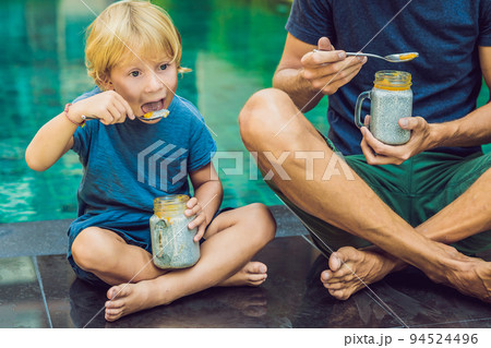 Father and son eat dessert with chia seeds and mangoes by the pool in the morning. healthy eating, vegetarian food, diet and people concept 94524496