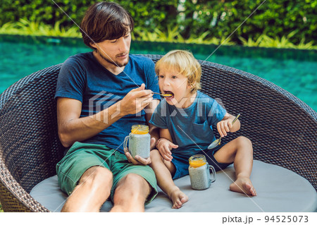 Father and son eat dessert with chia seeds and mangoes by the pool in the morning. healthy eating, vegetarian food, diet and people concept Father and son eat dessert with chia seeds and mangoes by the pool in the morning. healthy eating, vegetarian food, diet and people concept 94525073