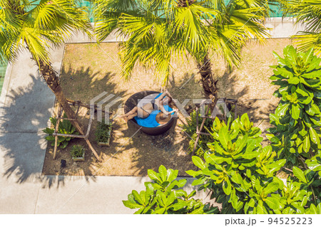 Girl in sun loungers among palm trees near the swimming pool 94525223