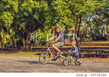 Happy family is riding bikes outdoors and smiling. Father on a bike and son on a balancebike Happy family is riding bikes outdoors and smiling. Father on a bike and son on a balancebike 94526298
