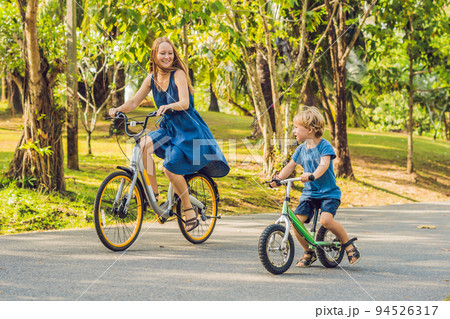 Happy family is riding bikes outdoors and smiling. Mom on a bike and son on a balancebike 94526317