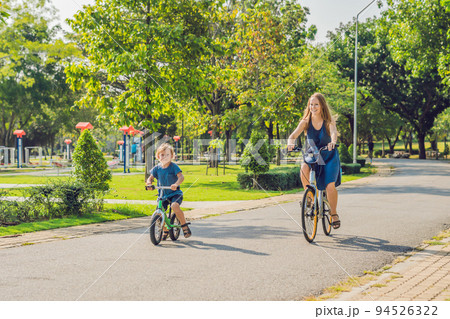 Happy family is riding bikes outdoors and smiling. Mom on a bike and son on a balancebike 94526322