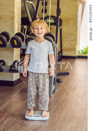 The boy stands on the scales to find out his weight The boy stands on the scales to find out his weight 94526405