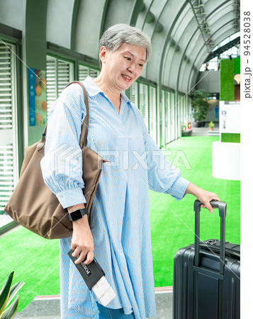 Portrait of senior adult elderly asian woman 60s smiling standing with suitcase luggage bag and holding passport with ticket for travel concept. 94528038