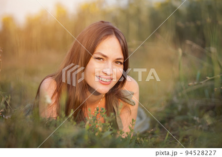Brown-haired woman lies on grass admiring meadow landscape 94528227