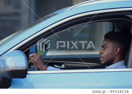 Serious African American driver sits in car cabin Serious African American driver sits in car cabin 94528238