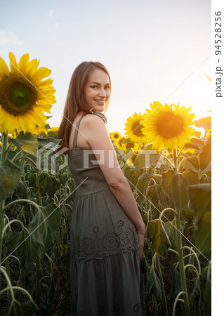 Woman in green dress walks past sunflower field on sunny day 94528256