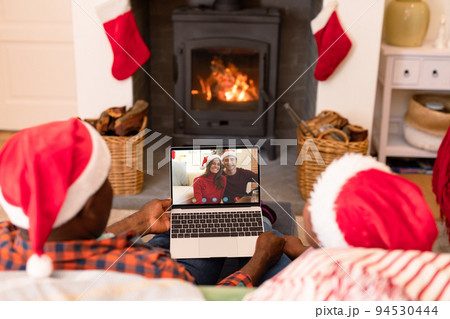 African american couple making laptop christmas video call with smiling caucasian couple African american couple making laptop christmas video call with smiling caucasian couple 94530444