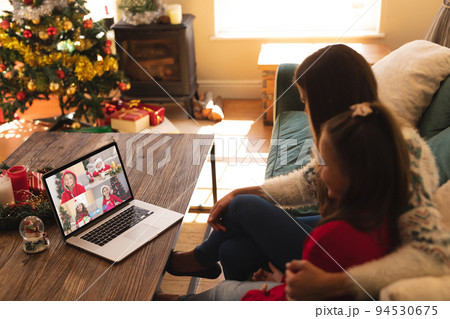 Caucasian mother and daughter in santa hat on christmas laptop video call with friends 94530675