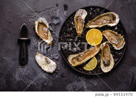 Opened fresh oysters on a plate, served with lemon and ice. 94531470