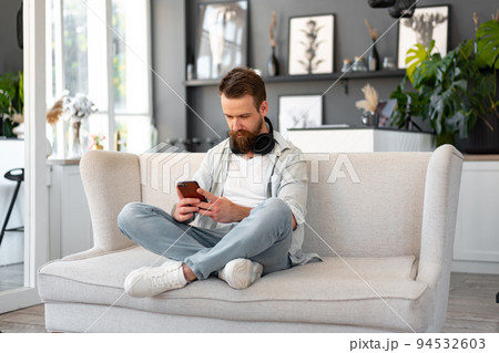 Handsome young bearded man spending time at home with phone in hands. 94532603