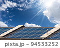 Many Solar Panels on a Roof against a Clear Sky with Clouds and Sunbeams 94533252