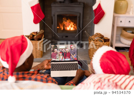African american senior couple in santa hats on laptop christmas video call with smiling family 94534370