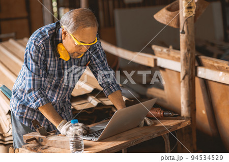 Senior builder wood worker using laptop computer at aiding design at construction work. Senior builder wood worker using laptop computer at aiding design at construction work. 94534529