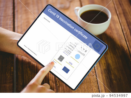 Hands of woman using tablet with covid vaccination certificate and qr code on screen 94534997