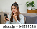 Pretty Asian girl using smartphone while relaxing in her living room. reading online blog 94536230