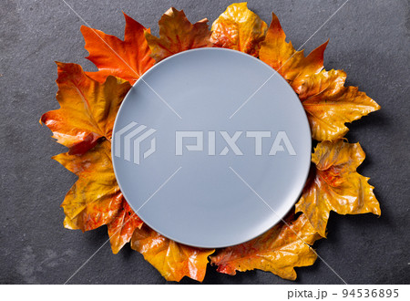 Overhead view of plate with autumn leaves decoration and copy space on grey background 94536895
