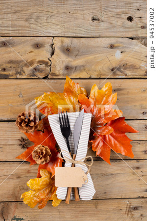 Overhead view of cutlery in napkin with autumn decoration and copy space on wooden background Overhead view of cutlery in napkin with autumn decoration and copy space on wooden background 94537002