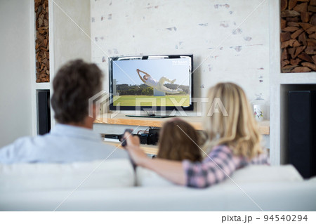 Rear view of family sitting at home together watching sport event on tv Rear view of family sitting at home together watching sport event on tv 94540294