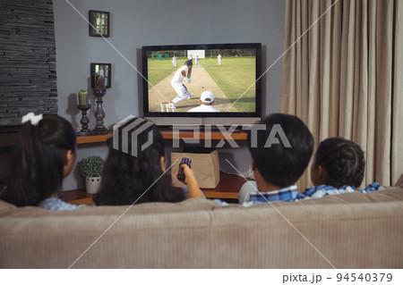 Rear view of family sitting at home together watching cricket match on tv Rear view of family sitting at home together watching cricket match on tv 94540379