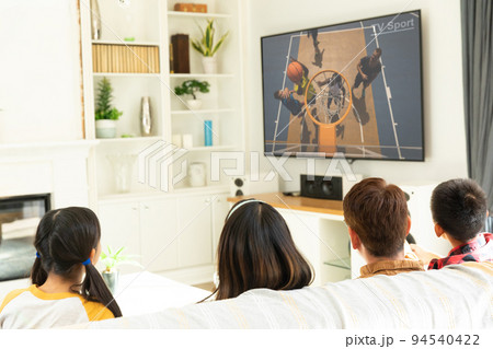 Rear view of family sitting at home together watching basketball match on tv Rear view of family sitting at home together watching basketball match on tv 94540422