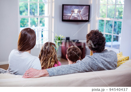 Rear view of family sitting at home together watching sport event on tv Rear view of family sitting at home together watching sport event on tv 94540437